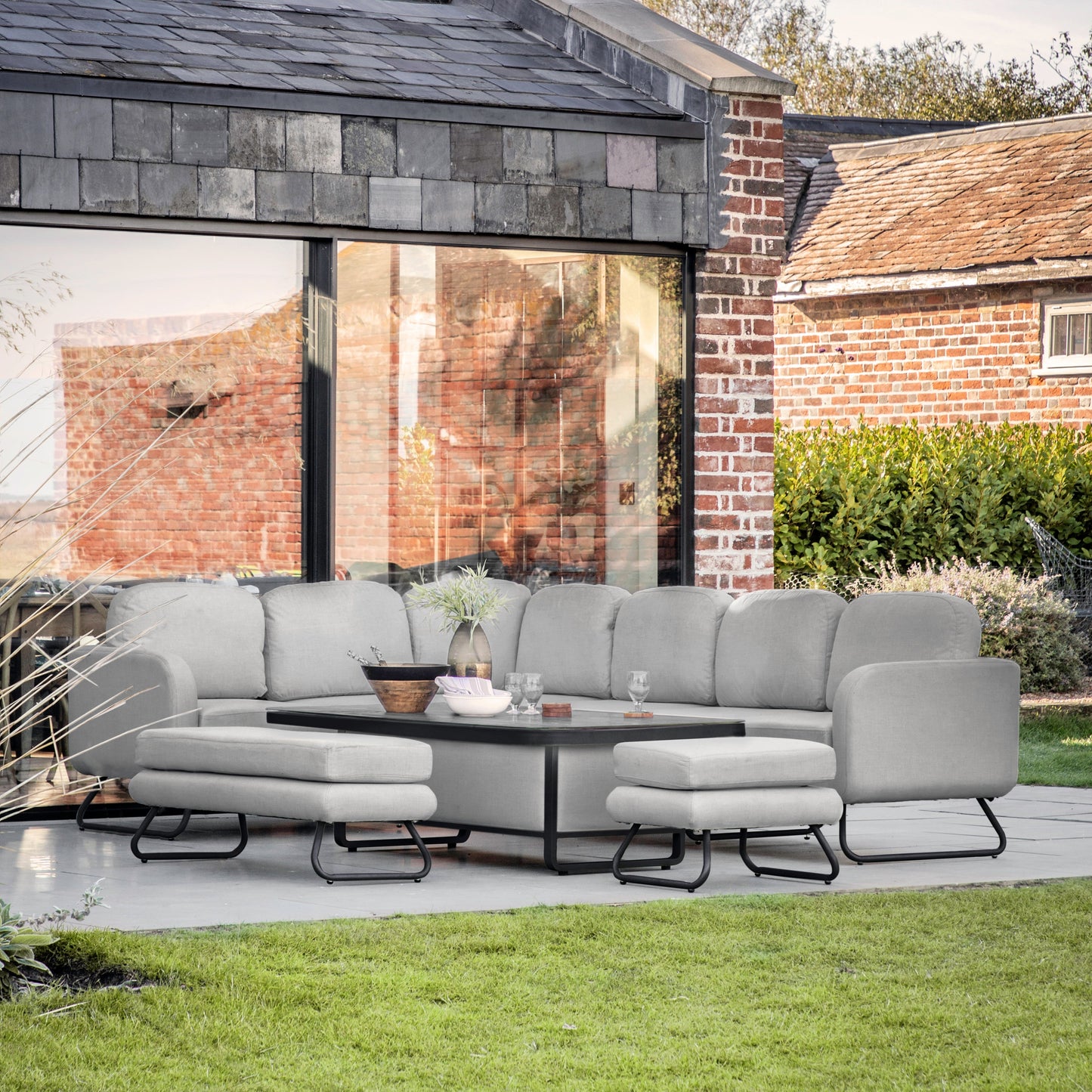 A grey Topsham Rectangle Dining Set Rising Table Slate sectional sofa set in a garden from Kikiathome.co.uk, perfect for interior decor.