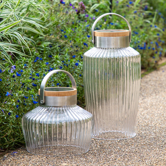 Two Averton LED Solar Lantern Small from Kikiathome.co.uk placed decoratively on a gravel path, adding a touch of interior decor to your outdoor space.