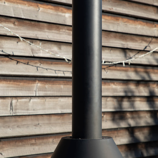 A Marldon Chiminea with Pizza Shelf, a stylish addition to your outdoor space from Kikiathome.co.uk, standing outside of a wooden building.