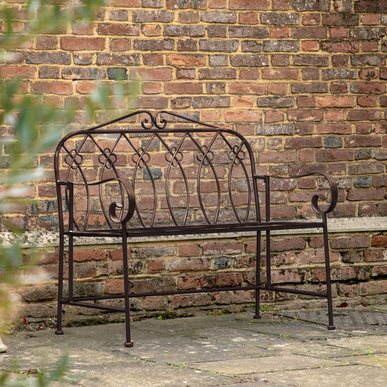 A Farringdon Outdoor Bench Noir in front of a brick wall, adding a touch of interior decor to any home.