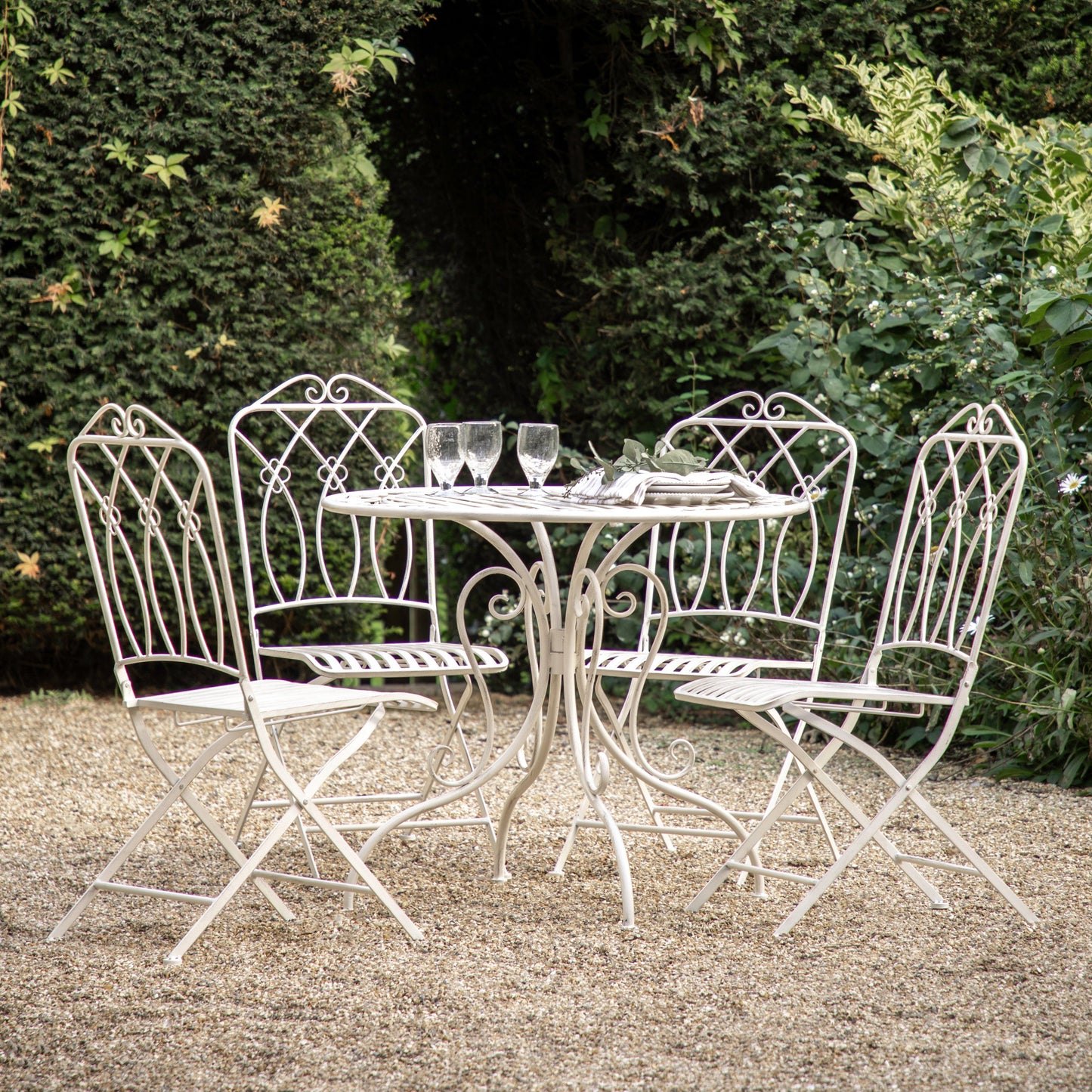 A Portlemouth 4 Seater Bistro Set Vanilla table and chairs in a garden from Kikiathome.co.uk, perfect for both interior decor and home furniture.