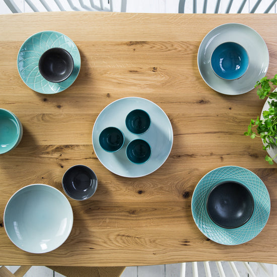 A Home furniture piece, A Farmhouse Rustic Oak Dining Table by Kiki, adorned with plates and bowls.