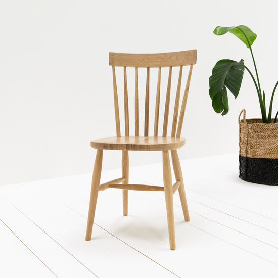 Home furniture: A pair of Kiki Oak Spindle Back Dining Chairs placed next to a potted plant as interior decor.